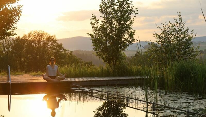 Frau meditiert am ruhigen Teich