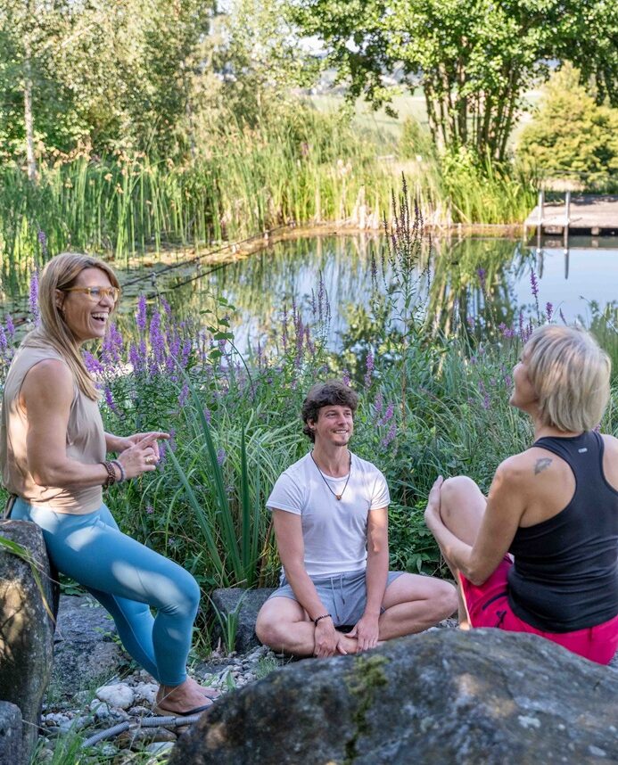 Drei Personen sitzen am Teich und reden.