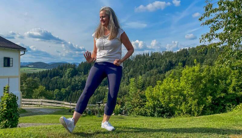 Frau, die Qi Gong ausführt mit Wiesen und Wäldern im Hintergrund